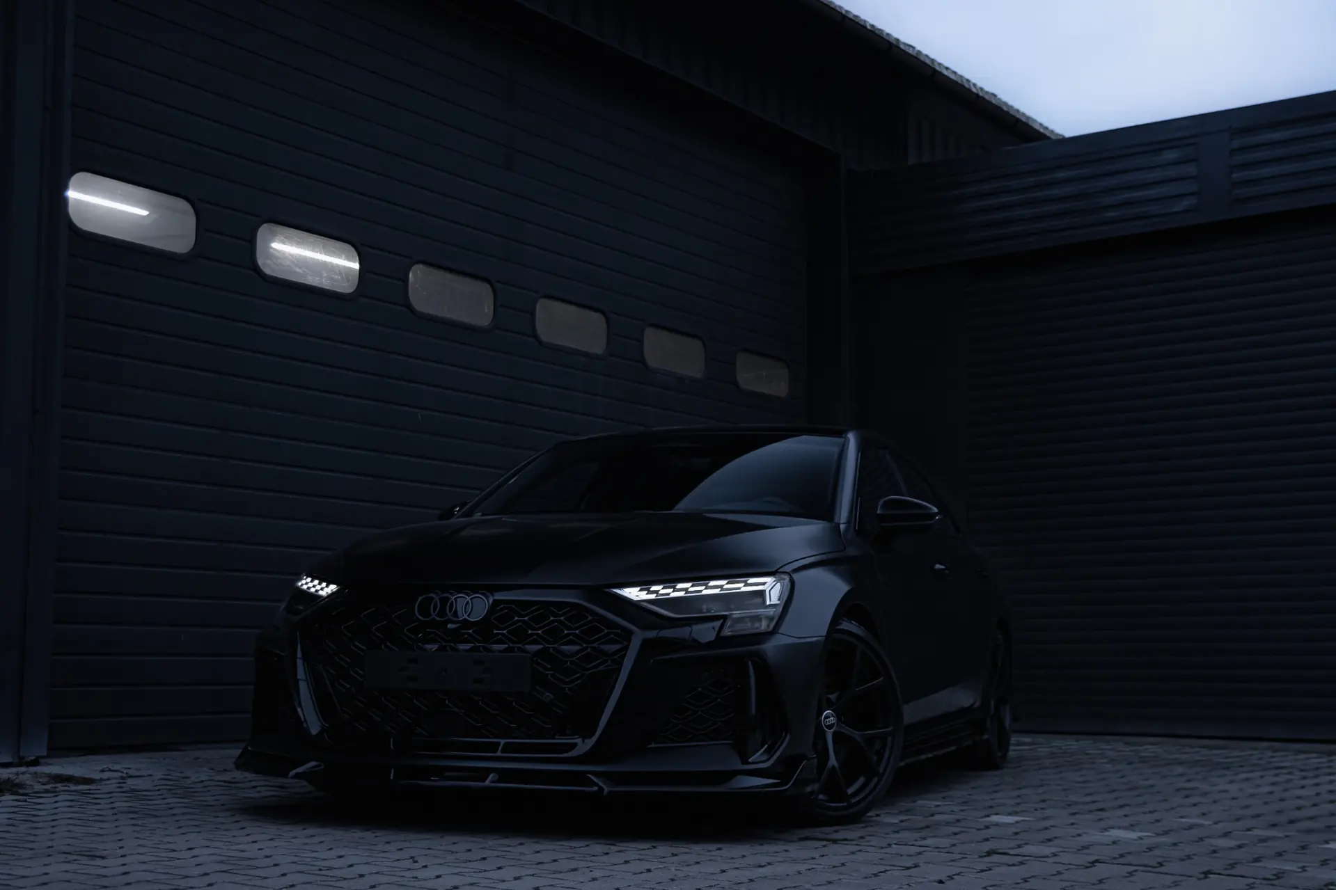Czarne Audi oklejone satynową folią PPF zaparkowane przed nowoczesnym garażem nocą